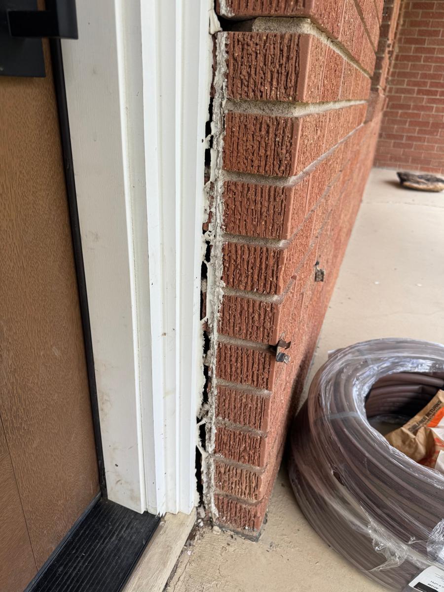 Brick veneer pulled away from the front door frame, with a coil of drip line on the porch