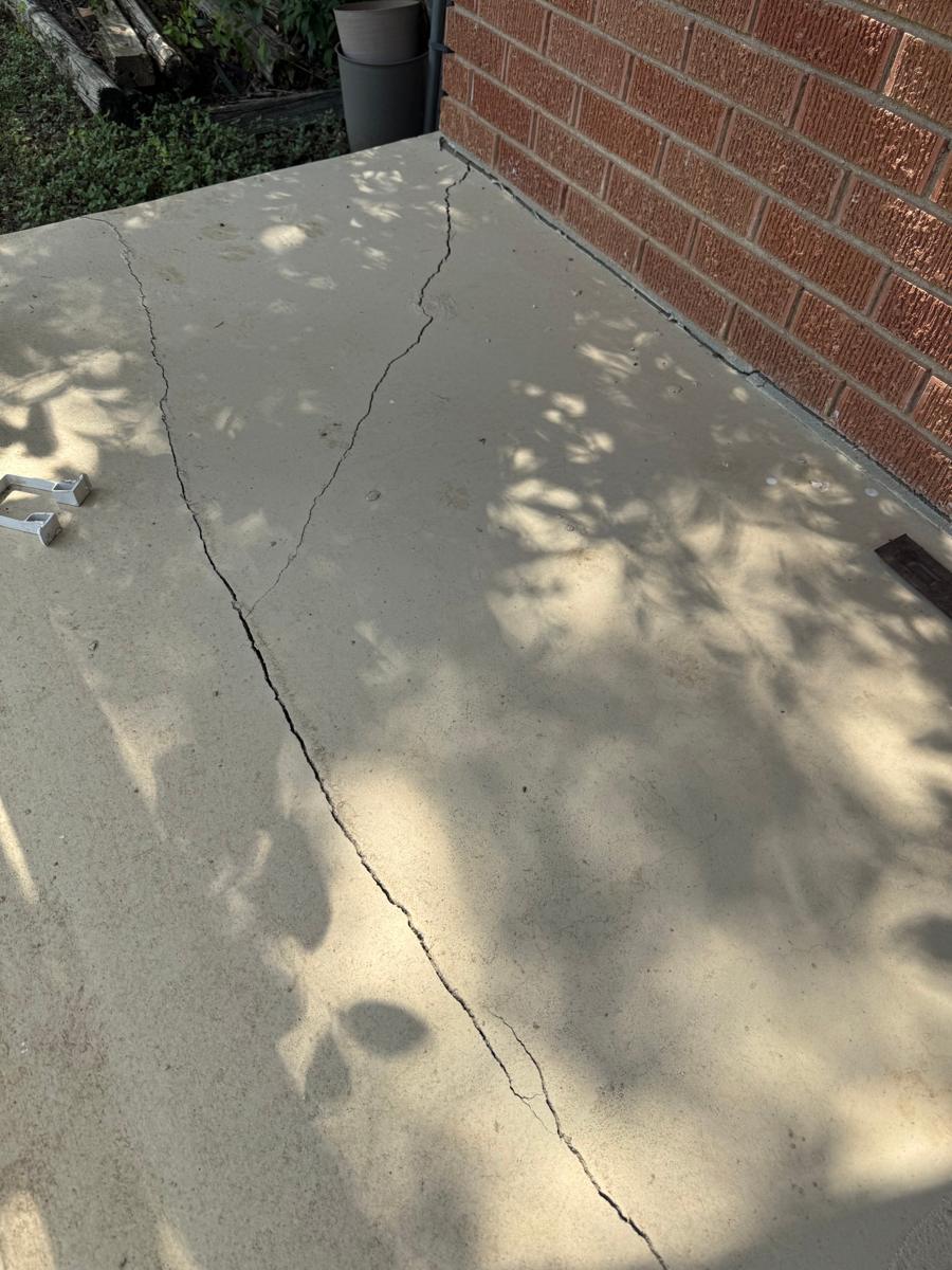 Long cracks across a concrete porch slab next to a brick wall